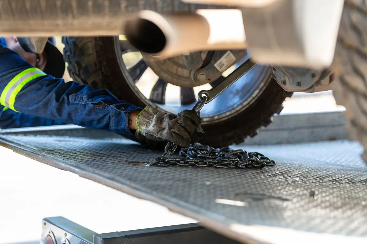 A gloved hand fastening a tow chain to a wheel on a flatbed deck
