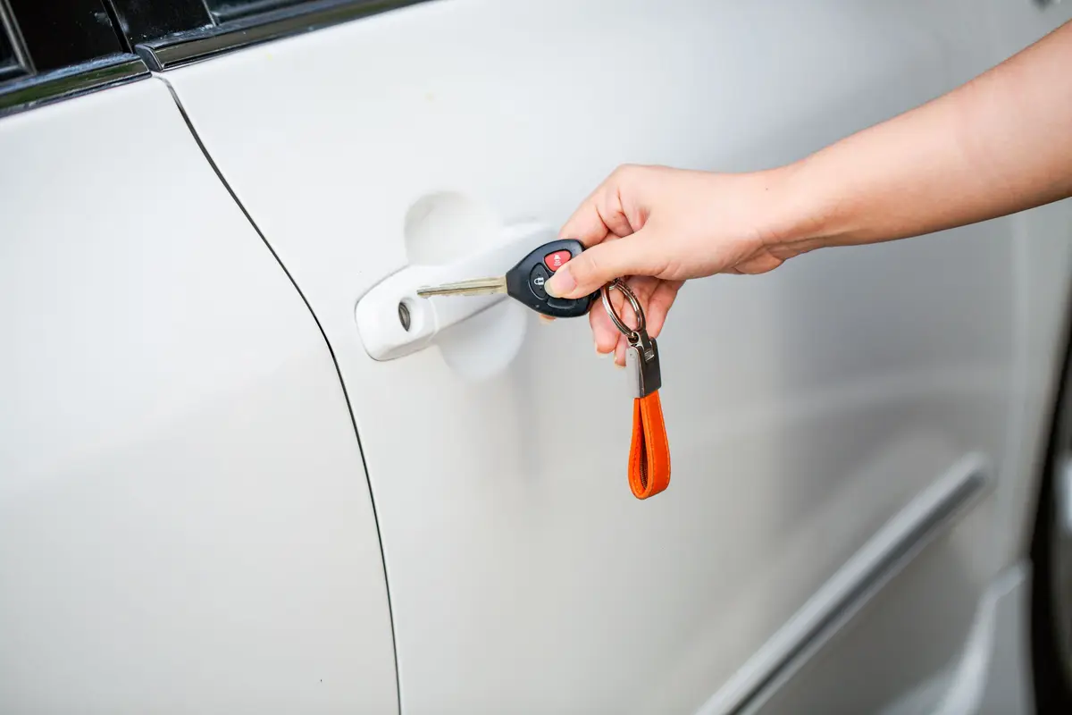 A hand holding a car key at the door handle of a white car