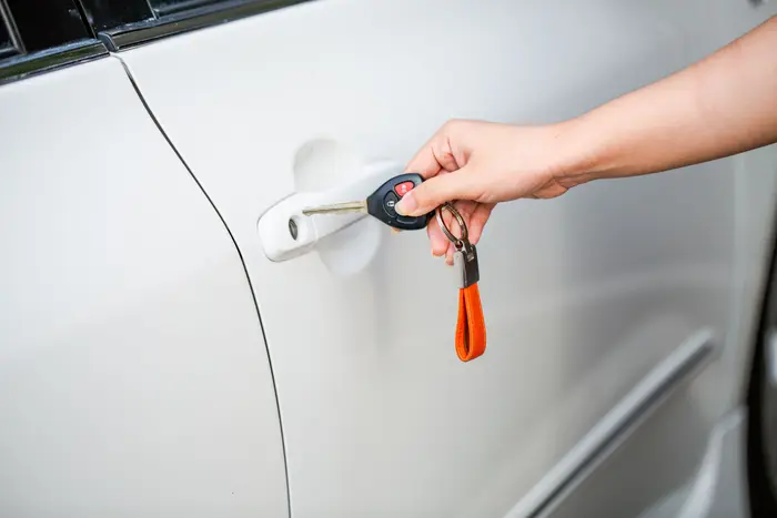 A hand holding a car key at the door handle of a white car