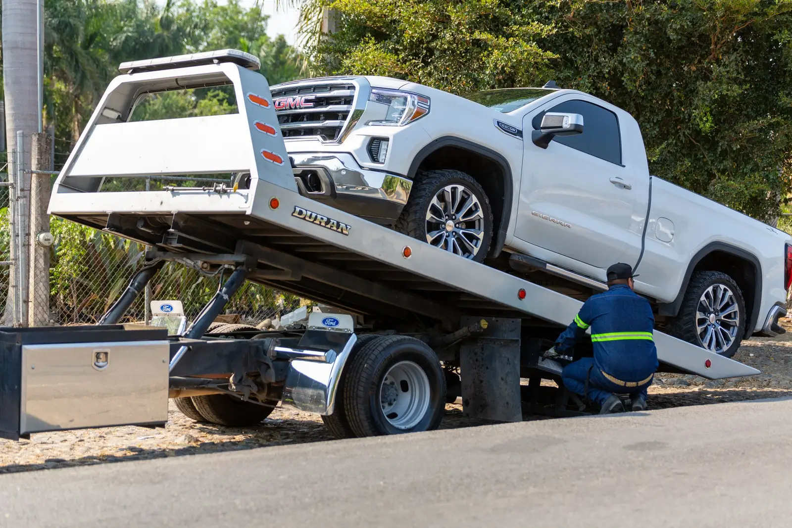 A white pickup winched onto the bed of a rollback tow truck