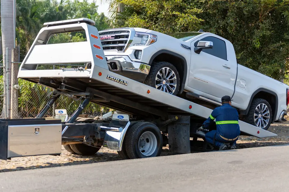 A white pickup winched onto the bed of a rollback tow truck